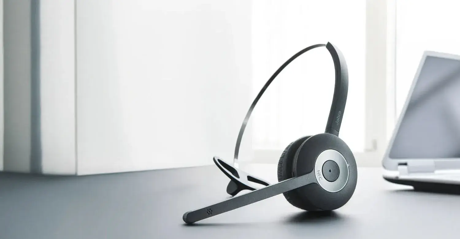 A sleek headset placed on a desk beside a laptop, representing the Device Catalogue for phones compatible with Now Reach, where users can explore detailed specifications and features to find the perfect business phone.