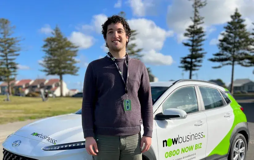 Male Now NZ employee standing in front of a company-branded car with Now Business logo and contact details, representing local expert support for health and wellness industry clients.
