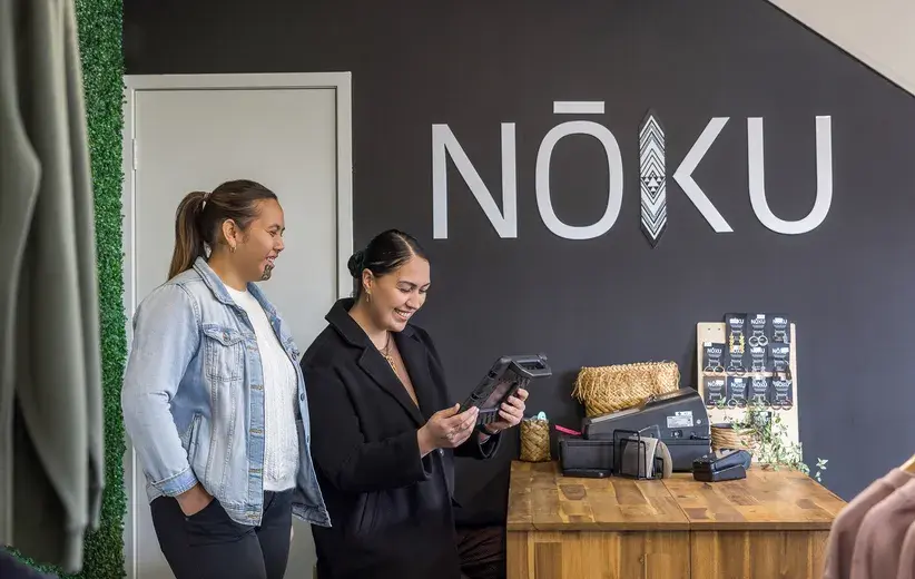 Two women in a Nōku store, one holding a tablet, symbolize the brand's reliance on top-notch broadband and support from Now to maintain both their online and physical stores' operations.