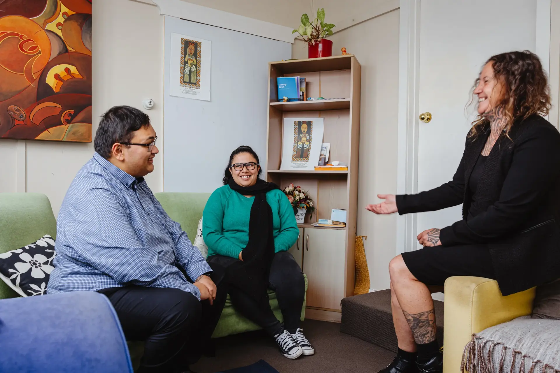 Three people from the Hawke's Bay Gambling Service engage in a warm and supportive discussion in a cozy, art-filled room. The organisation relies on Now's reliable telecommunications services to effectively carry out their important community work, ensuring seamless communication and connection.