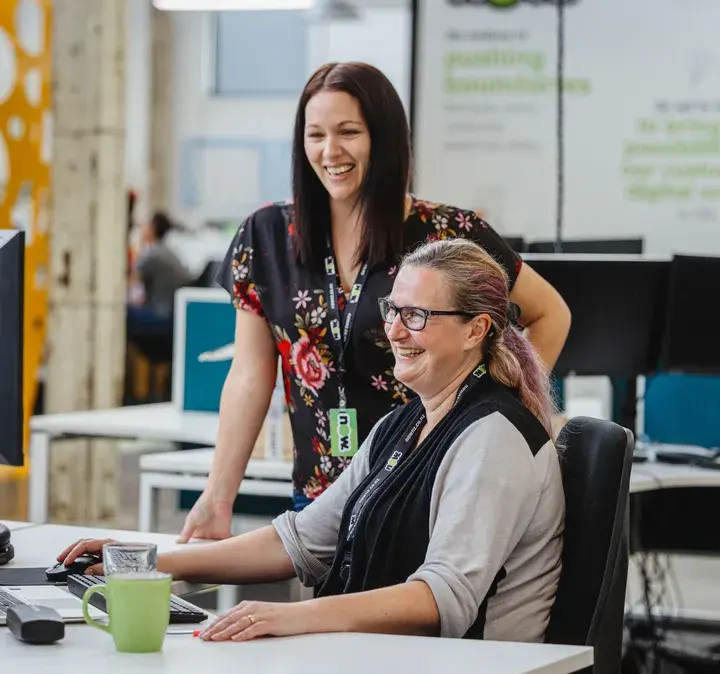 Two women smiling and working together at a desk in a modern office setting, highlighting the Reach Call Centre by Now. Ideal for small to medium businesses, Now Reach Call Centre offers all the capabilities a service-led organisation needs without unnecessary costs or complexities.