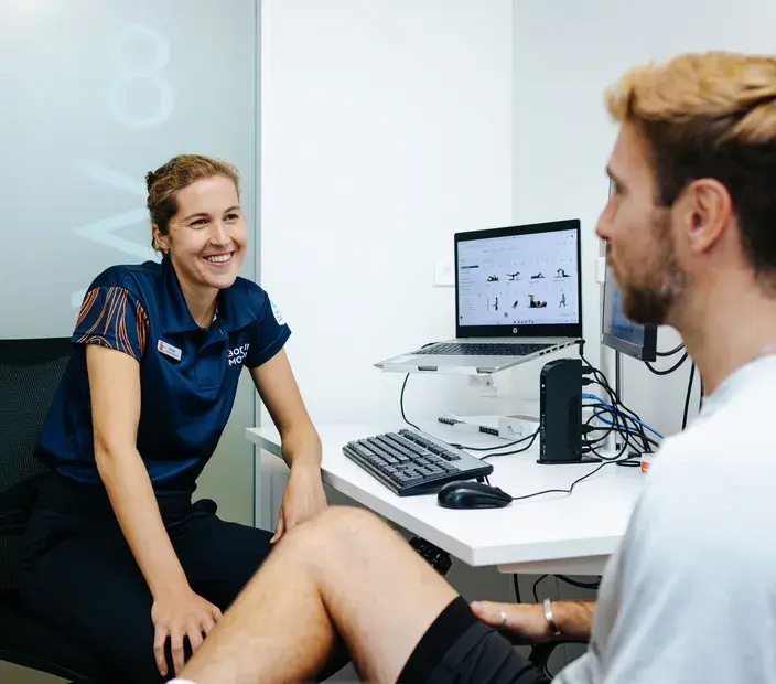 Female physiotherapist smiling and talking to a male patient in a clinic, illustrating Body in Motion's partnership with Now NZ for critical customer call management in healthcare services.