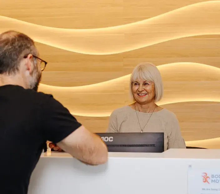 Receptionist smiling and assisting a customer at the Body in Motion healthcare clinic, highlighting the importance of reliable customer call handling in healthcare